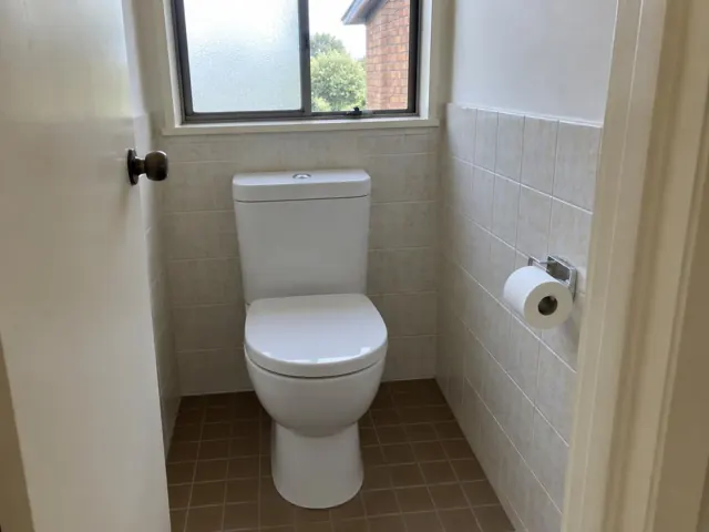 Clean white toilet in a tiled small bathroom with a window and paper holder in Cromer