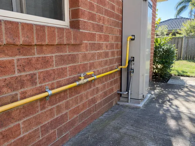 Yellow gas piping along a brick exterior wall beside a utility meter and driveway in Beacon Hill