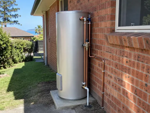 Outdoor hot water system beside a brick house wall with copper pipework and drain line in Narrabeen