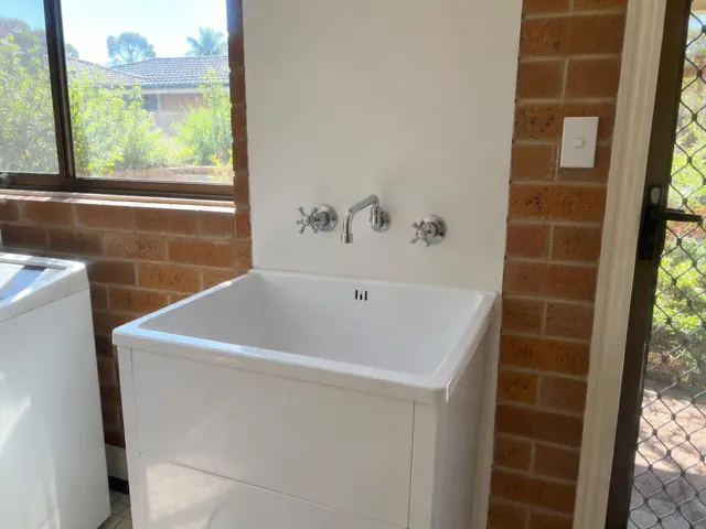 White laundry sink with new tap against brick wall and window in Dee Why